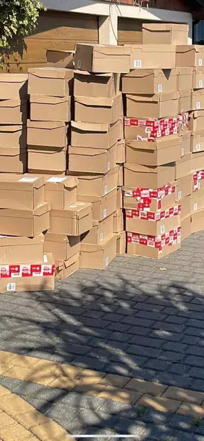 Shoe boxes stacked higher than a person on a driveway